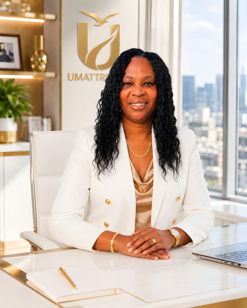 Lornette Daye seated at an executive desk in a white blazer with the UMattr crest behind her.